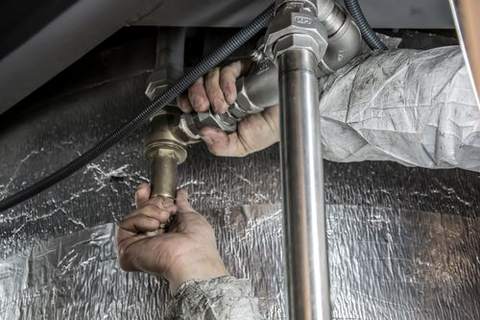 A plumber working on pipes under a sink